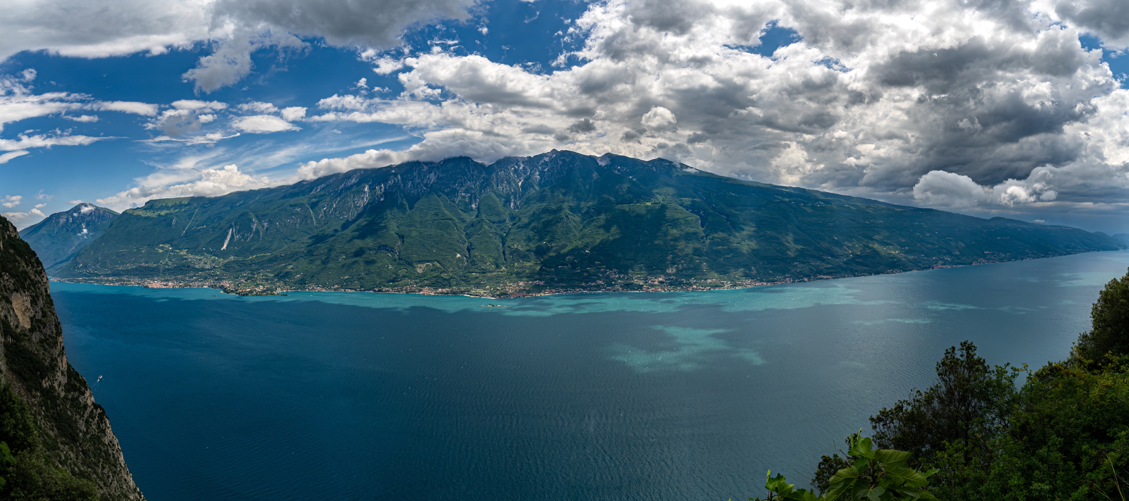Panorama du lac de Garde avec vue sur la côte montagneuse et la surface bleue de l'eau sous un ciel spectaculaire avec des nuages dynamiques.