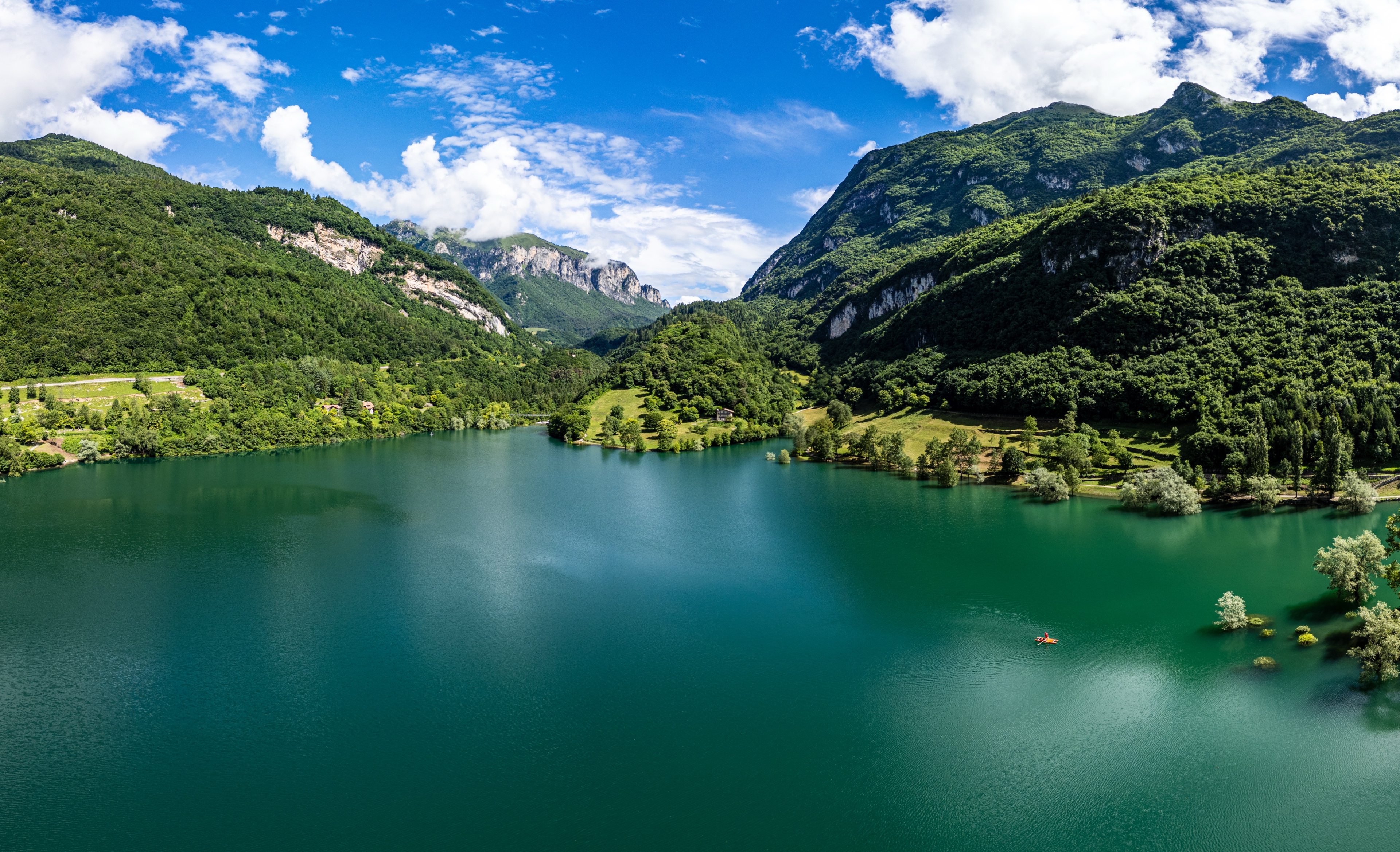 Le lac Tenno, photographié depuis un drone – entouré de collines verdoyantes et de montagnes, avec ses eaux turquoise et un petit bateau visible à droite.