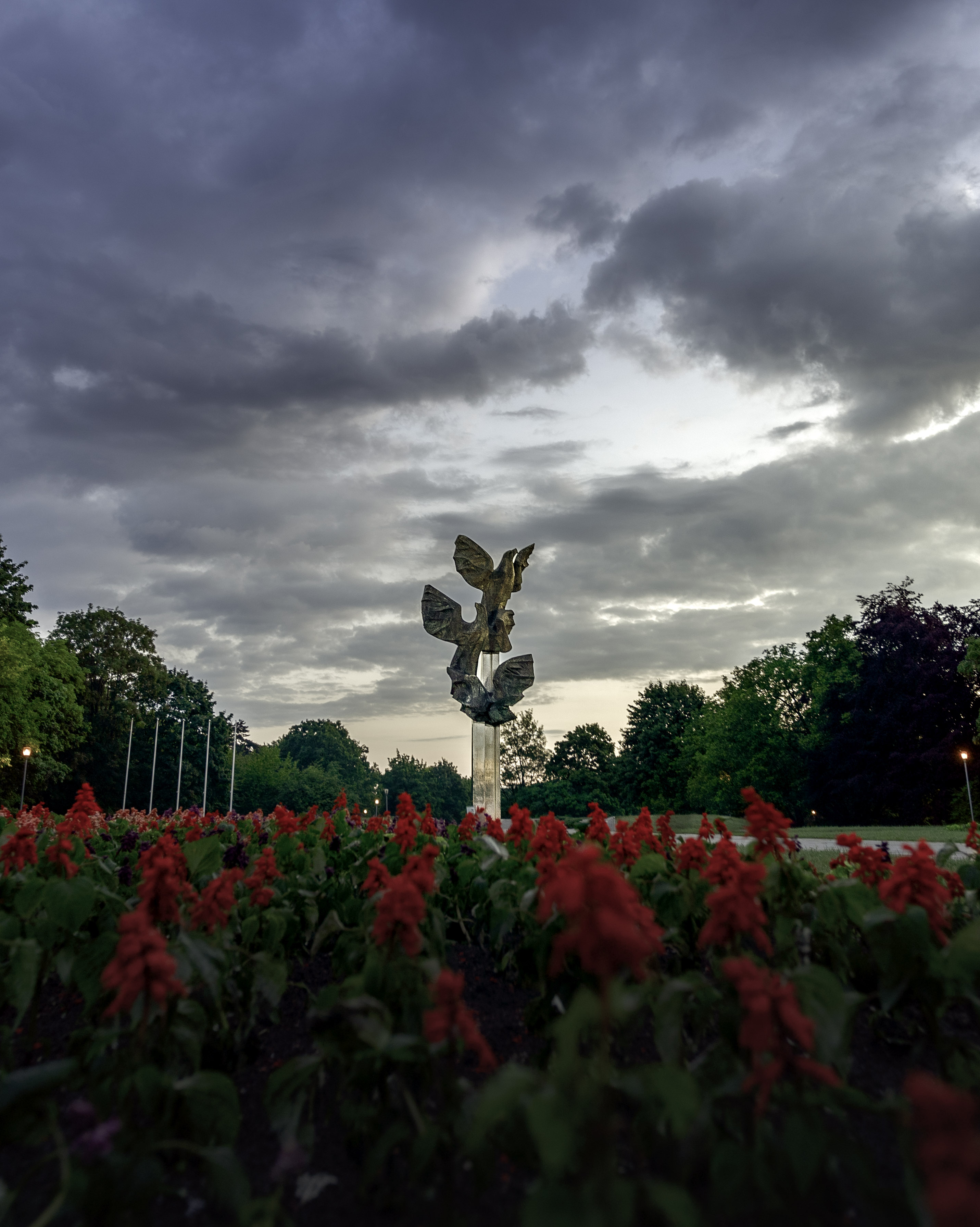 Le monument dédié aux exploits des Polonais à Szczecin, photographié depuis un angle bas, avec en arrière-plan des fleurs rouges et un ciel spectaculaire au crépuscule.