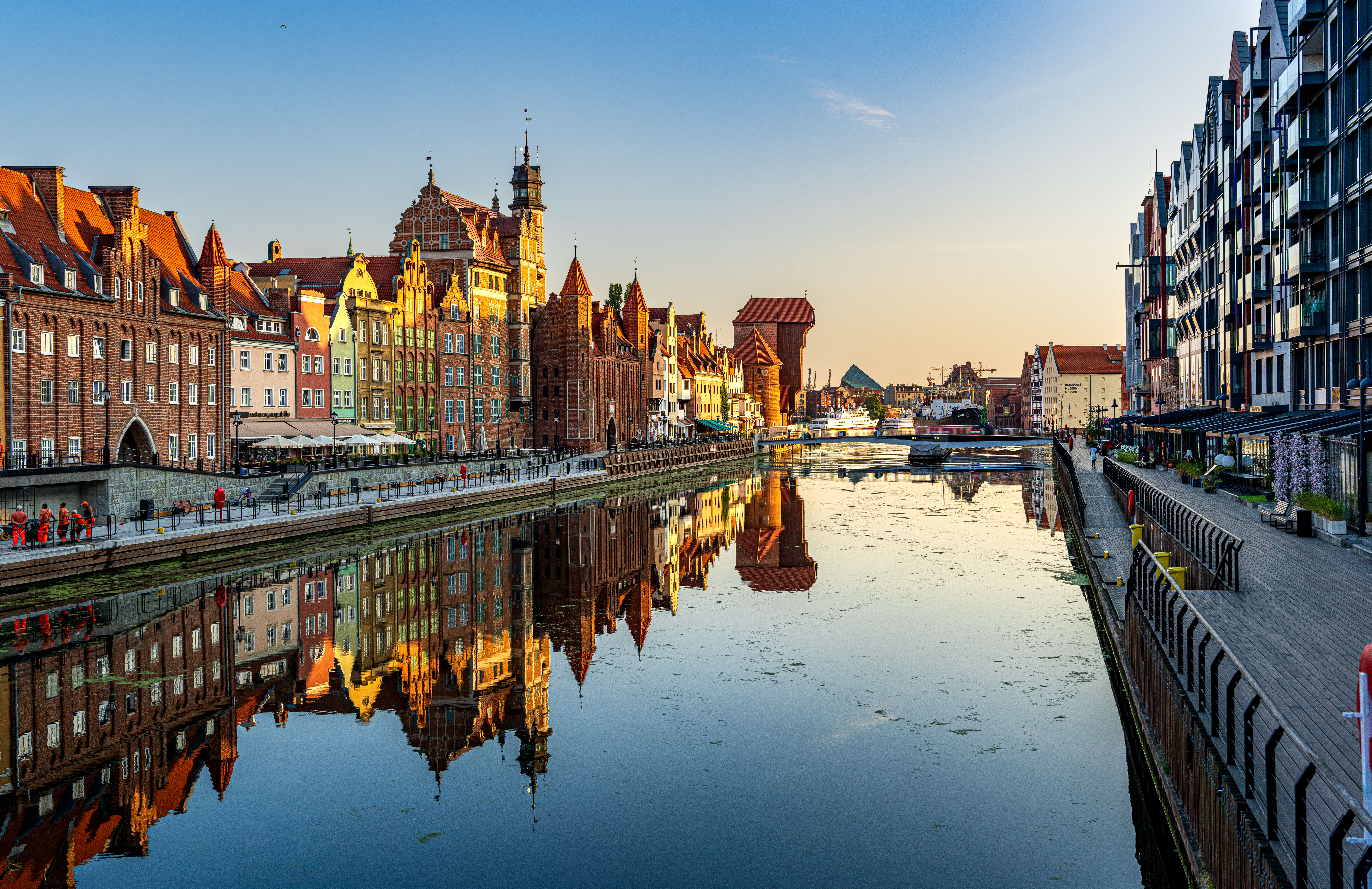 Panorama de la vieille ville de Gdańsk à l'heure dorée, avec ses immeubles historiques qui se reflètent dans la surface calme de la Motława.