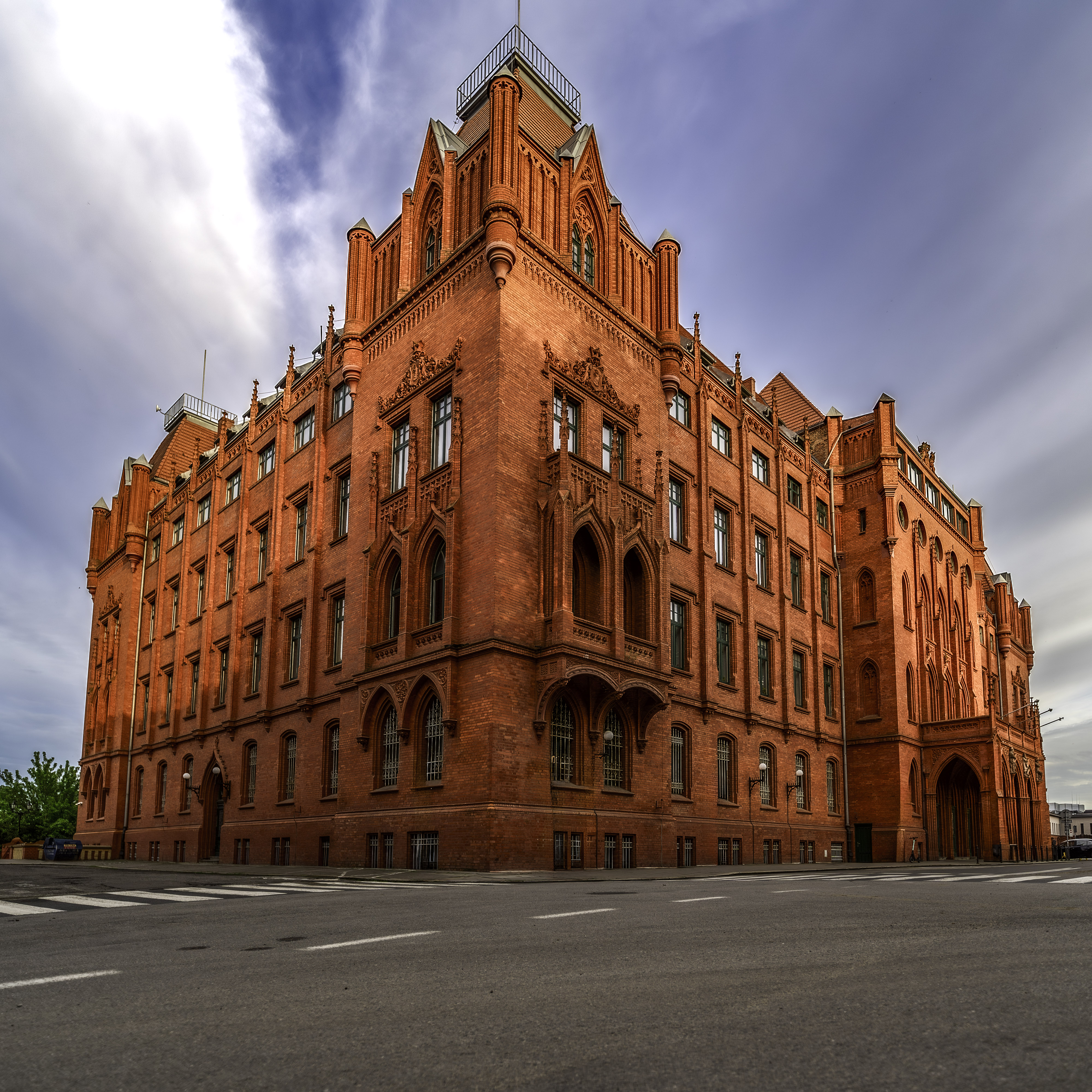 L'hôtel de ville néogothique rouge de Szczecin, avec sa façade en briques d'un rouge intense, actuellement siège de l'administration maritime ; vue d'angle sous un ciel nuageux.